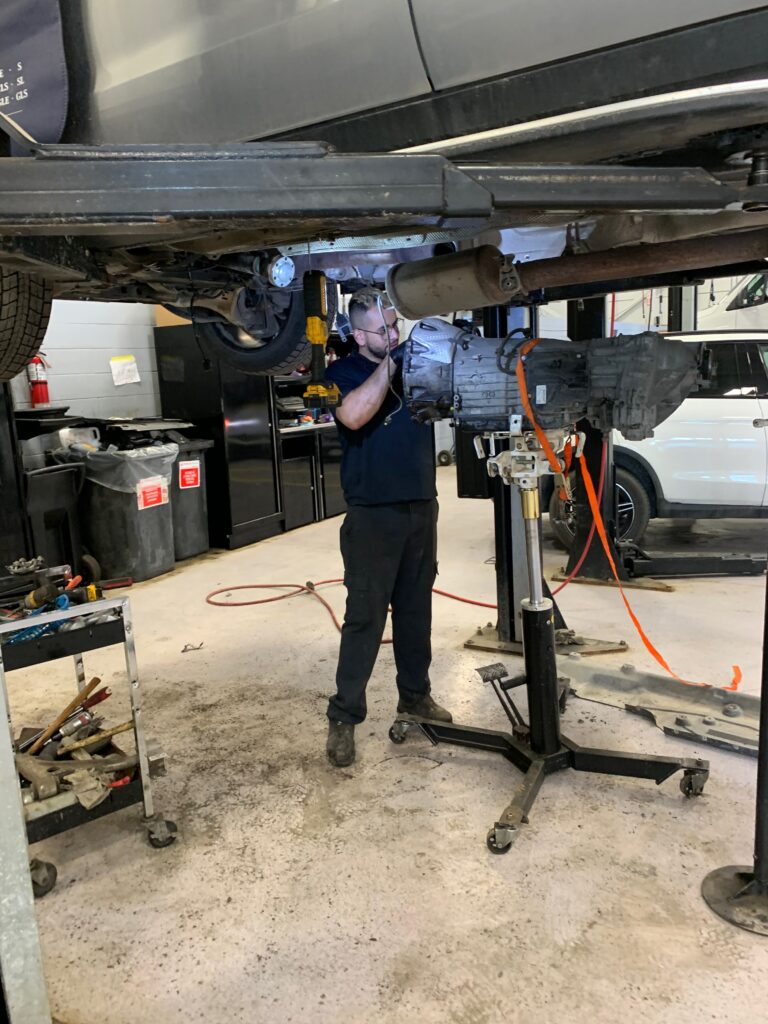 Technicien automobile travaillant sous un véhicule surélevé pendant une intervention mécanique en atelier.